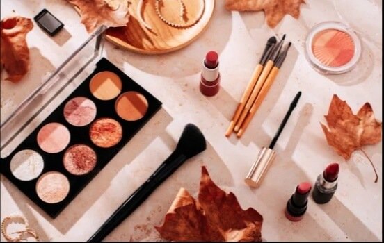 "Beauty product such as Eyeshadow palette, makeup brushes, lipsticks, and dry autumn leaves on a textured surface"